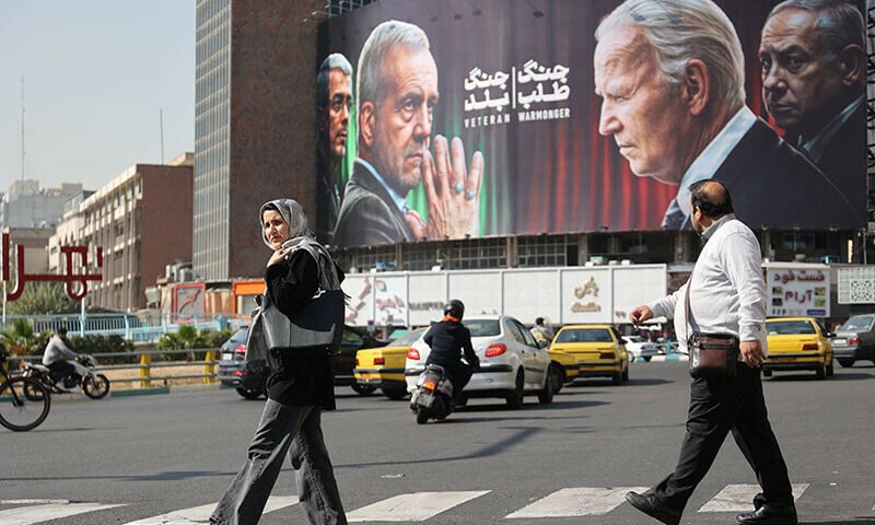 iranians walk next to an anti us and israeli billboard with pictures of iranian president masoud pezeshkian and iranian armed forces chief of staff major general mohammad bagheri and u s president joe biden and israel s prime minister benjamin netanyahu on a street in tehran iran photo reuters