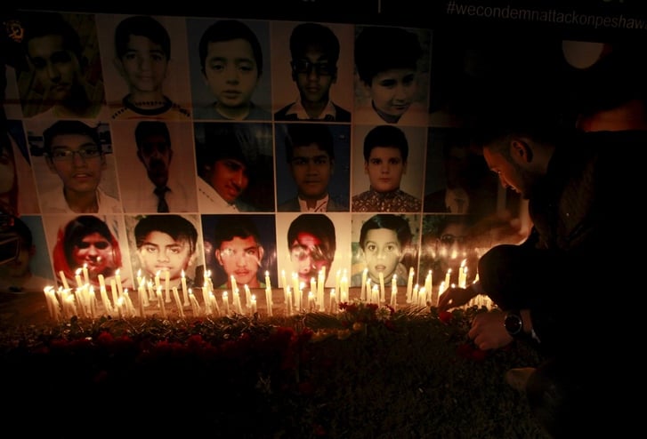 a man places a rose after lighting candles in front of portraits of the victims of the taliban attack on the army public school in peshawar during a candlelight vigil in lahore in this december 19 2014 file photo photo reuters