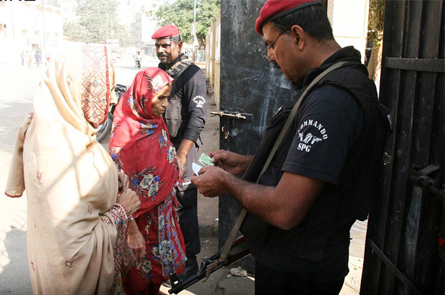 a policemen checking the identity card of the women on the entrance of a polling station photo online