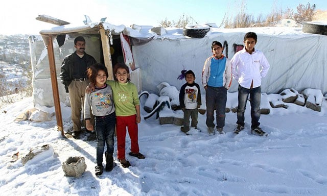 syrian refugees pose in the snow in front of their makeshift home photo afp