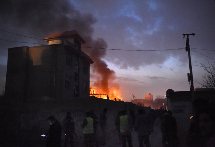 security personnel and bystanders look on as flames and smoke rise at the site of a suicide car bomb attack at a french restaurant  le jardin in kabul on january 1 2016 photo afp