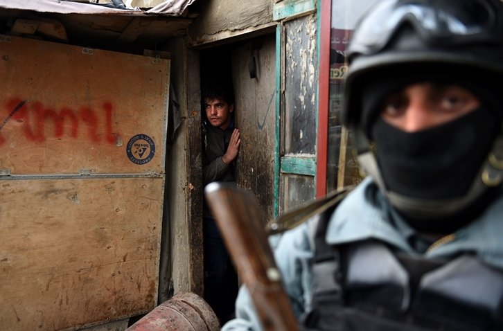 an afghan resident peers out of the doorway of his house as an afghan policeman keeps watch at the site of a suicide bomb attack near the international airport in kabul on january 4 2016 photo afp