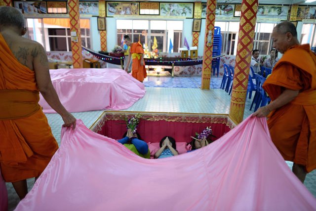 this picture taken on january 16 2016 shows buddhist monks draping a pink sheet over members of a family lying in a large coffin during a group resurrection ceremony at the wat ta kien buddhist temple in nonthaburi on the outskirts of bangkok photo afp