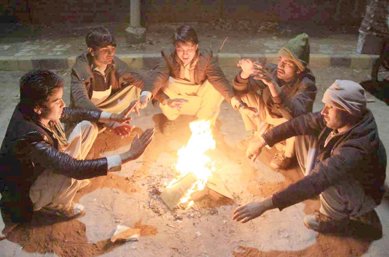 boys huddled around a small bonfire trying to warm their hands in lahore photo nni