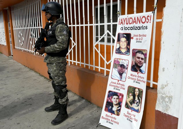 a civil forces police stands next to a banner with pictures of five youngsters who went missing past january 11 in tierra blanca community veracruz state mexico on january 25 2016 photo afp