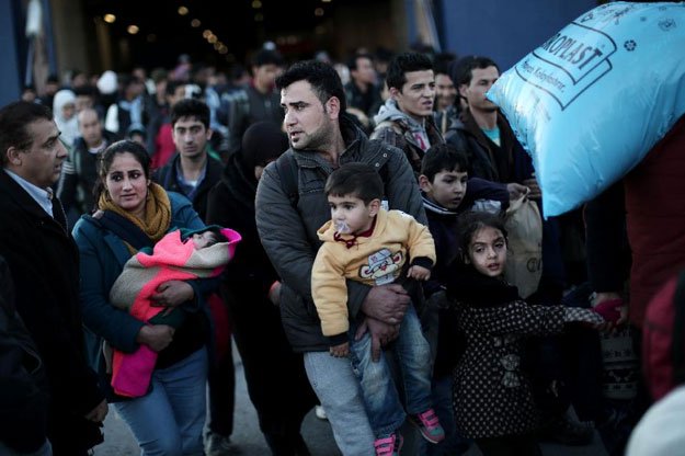 a migrant man carries a baby as refugees and migrants disembark from the passenger ferry blue star arriving from the island of lesbos at the port of piraeus on january 31 2016 in athens photo afp