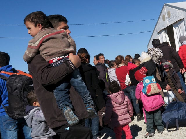 a migrant carries a child as refugees and migrants wait for a train to continue their journey towards western europe from the macedonia greece border at the vinojug temporary transit centre outside the village of gevgelija macedonia february 1 2016 photo reuters