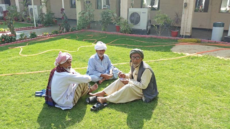 elderly passenger ameer buksh right sits with two other stranded umrah passengers in the lawn of airport hotel on wednesday their flight was cancelled three hours after its scheduled departure photo express