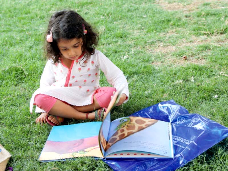 a little girl flips through her book in the beach luxury lawn at the literature festival on friday