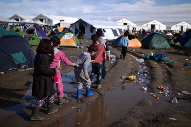 children walk along a puddle at a makeshift camp after night 039 s rainfall near the greek village of idomeni at the greek macedonian border on march 4 2016 where thousands of migrants and refugees are stranded photo afp