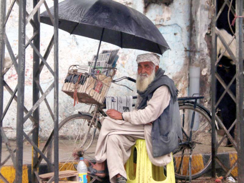 a man sits under an umbrella during rains in the city photo muhammad iqbal express