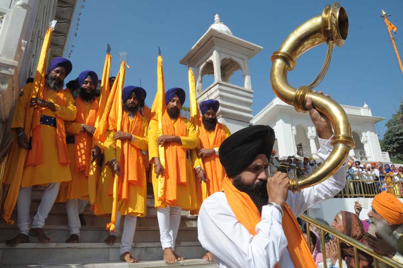 an indian sikh devotee plays a musical instrument as he walks with punj pyara holding flags of the sikh religion during a procession from sri akal takhat at the golden temple in amritsar on november 5 2014 on the eve of the 545th birth anniversary of sri guru nanak dev photo afp