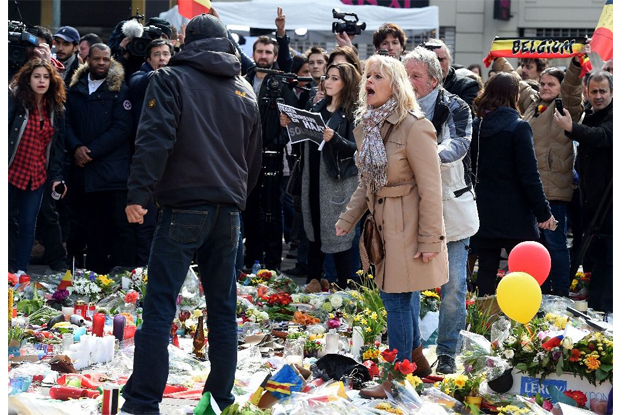 a woman shouts at a man walking amongst floral tributes in area outside the stock exchange in brussels on march 27 2016 photo afp