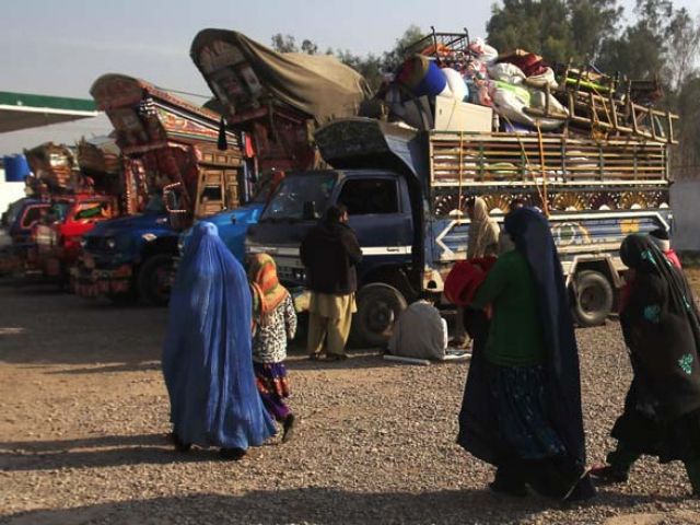 an afghan refugee family walks past trucks loaded with their belongings as they prepare to go back to afghanistan with others at the unhcr office on the outskirts of peshawar february 13 2015 photo reuters