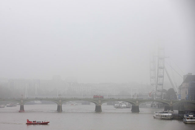 a boat travels along the river thames as fog shrouds the london eye r in central london on november 2 2015 photo afp