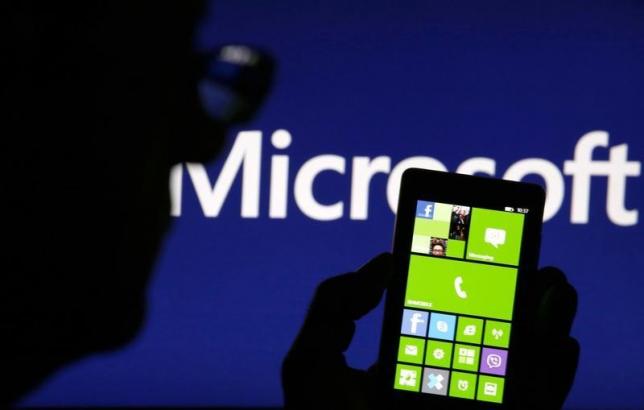 a man is silhouetted against a video screen with the microsoft logo in the background as he poses with a nokia lumia 820 smartphone photo reuters