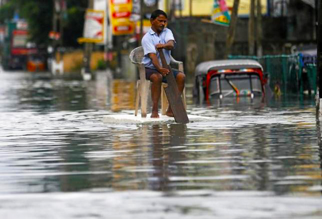 a man sits on a chair as he uses a piece of styrofoam to move through a flooded road in wellampitiya sri lanka may 21 2016 photo reuters