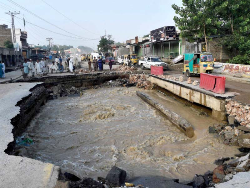 residents gather beside a road damaged by floodwaters following heavy downpours photo afp