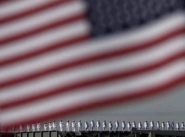 the crew members of the uss ronald reagan a nimitz class nuclear powered super carrier saluting is seen behind the national flag of the us as it arrives at the us naval base in yokosuka south of tokyo japan october 1 2015 photo reuters