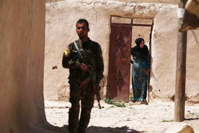 a syria democratic forces sdf fighter stands near a woman looking out a doorway in a village on the outskirts of manbij city after they took control of it from islamic state forces aleppo province syria june 8 2016 photo reuters