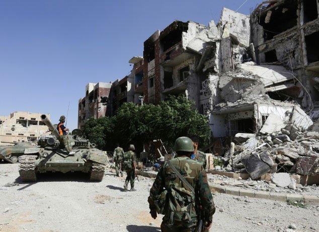 a syrian government tank is parked near damaged buildings as soldiers walk past in adra northeast of the capital damascus on september 25 2014 photo afp file