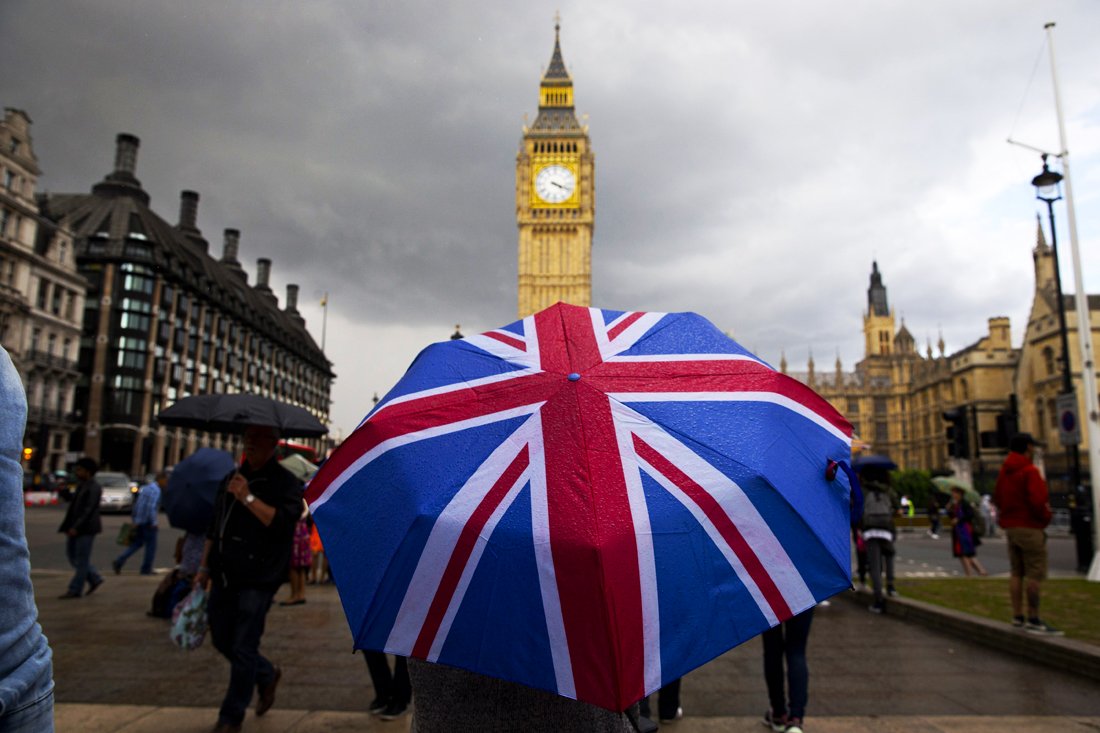 a pedestrian shelters from the rain beneath a union flag themed umbrella as they walk near the big ben clock face and the elizabeth tower at the houses of parliament in central london on june 25 2016 following the pro brexit result of the uk 039 s eu referendum vote photo afp