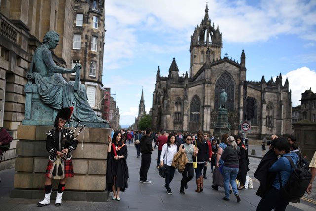 a street performer plays the bagpipes next to a statue of scottish philosopher david hume on the royal mile in edinburgh scotland on june 25 2016 photo afp oli scarff