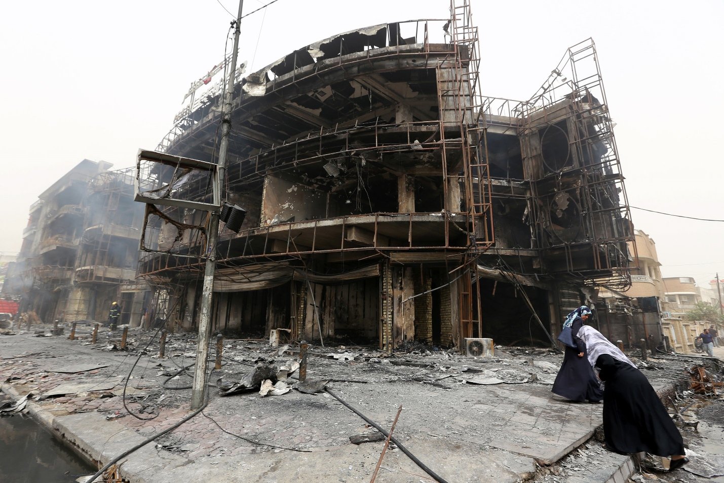 iraqi women walk past a damaged building at the site of a suicide car bombing claimed by the islamic state group on july 3 2016 in baghdad 039 s central karrada district photo afp