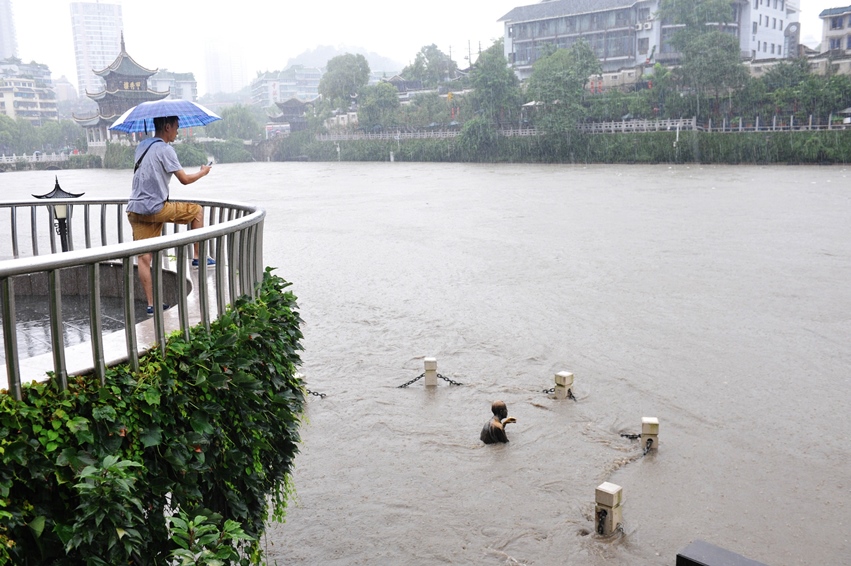 this picture taken on july 16 2014 shows a man l taking a photo of a statue bottom submerged in floodwaters in guiyang in southwest china 039 s guizhou province photo afp