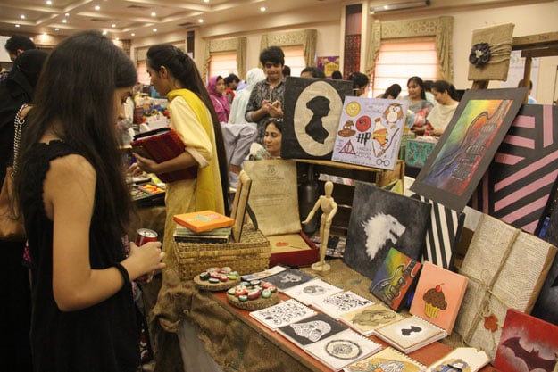 a girl is photographed looking at the art work displayed at one of the stalls