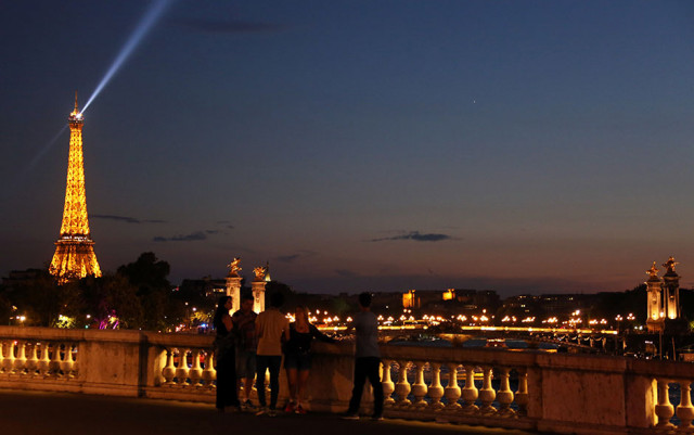 this picture taken from concorde bridge over the river seine in paris shows a group of young people looking at the eiffel tower the alexandre iii bridge and night lights of the city photo afp