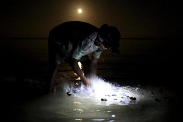a fisherman uses a headlight while cleaning a fishnet before loading it on his small boat as the moon sets down at a shore in mogpog town marinduque island central philippines april 3 2015 photo reuters