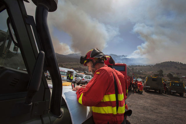 members of the military emergency unit ume look at a map of the island of la palma at a field emergency post set up on the outskirts of the town of el paso on the spanish canary island of la palma on august 4 2016 as smoke from a wildfire rises skywards in the background photo afp