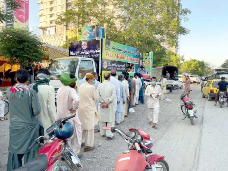 people form a queue to collect cooked meals from the newly inaugurated mobile restaurant in the federal capital photo express