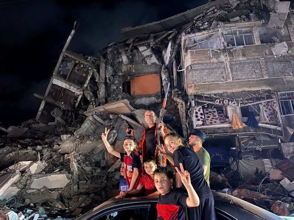 People gesture near the rubble of a damaged building as Palestinians celebrate in the streets following a ceasefire, in Gaza City May 21, 2021. PHOTO: REUTERS