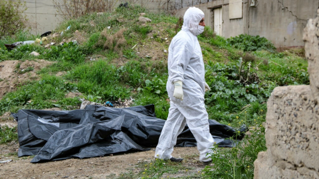 a worker walks past the covered remains of bodies unearthed from a mass grave in the northern iraqi city of mosul afp a worker walks past the covered remains of bodies unearthed from a mass grave in the northern iraqi city of mosul afp