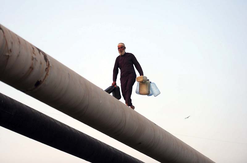 an elderly man walks on a water pipeline carrying empty containers a severe water crisis hit the city after the main trunk line at dhabeji pumping station was damaged due to load shedding on tuesday photo file