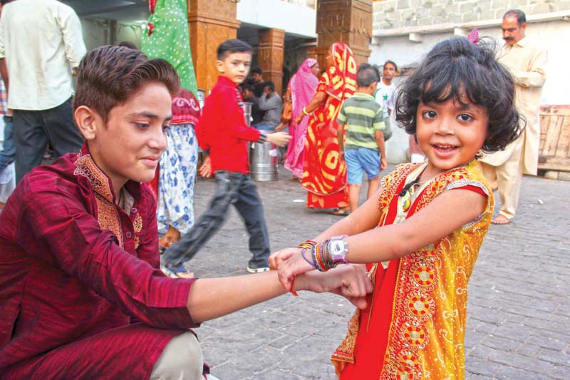 a little girl ties a rakhi on the wrist of her brother left while women check the variety of rakhis offered at lakshmi narayan mandir on thursday right photos ayesha mir express