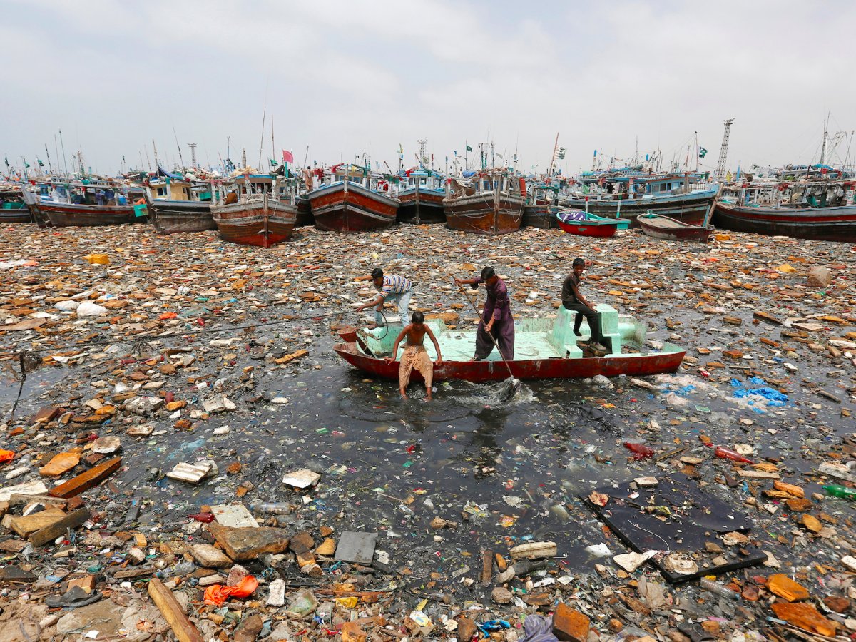 boys aboard an abandoned boat collect recyclable items through polluted waters in front of fishing boats at fish harbor in karachi pakistan august 17 2016 photo reuters