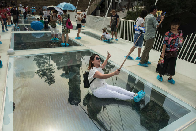 a tourist takes a photograph on the world 039 s highest and longest glass bottomed bridge above a valley in zhangjiajie in china 039 s hunan province on august 20 2016 photo afp