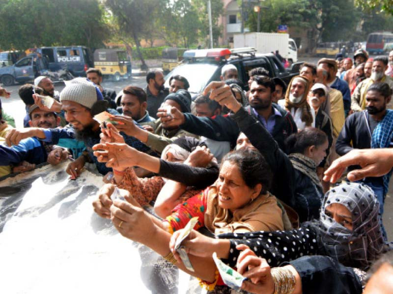 people made to stand in a queue by a police mobile squad hold cash in hands to buy subsidised flour bags at a sale point in karachi photo express