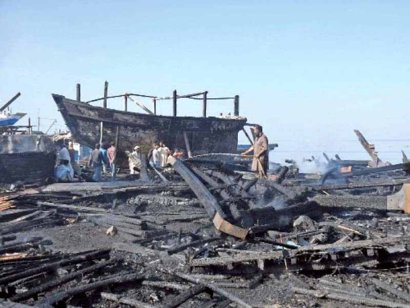 people stand at the jetty of karachi fish harbour where dozens of boats were gutted due to fire photo online