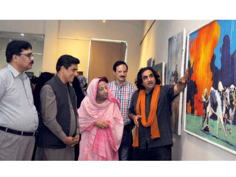 an artist explains his painting to art enthusiasts during an exhibition at the pac photo express