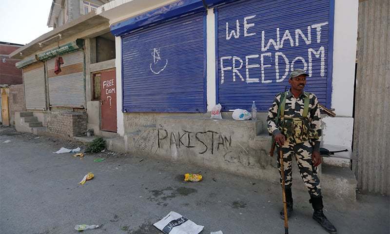 a policeman stands guard near shops painted with graffiti during a curfew in srinagar photo rueters