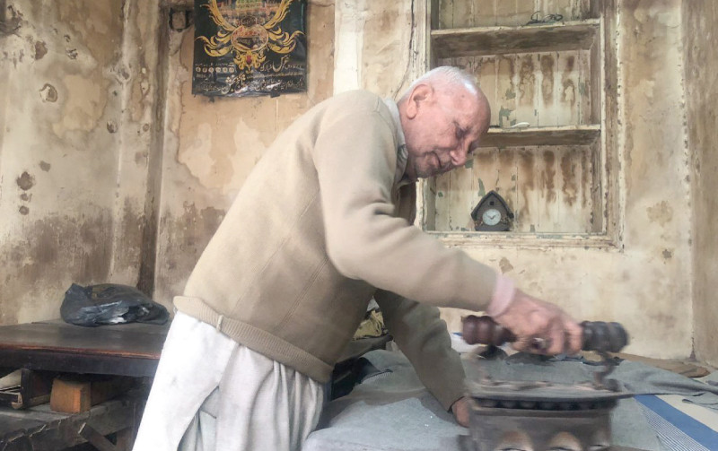 an old man irons clothes with a charcoal iron in islamabad photo express