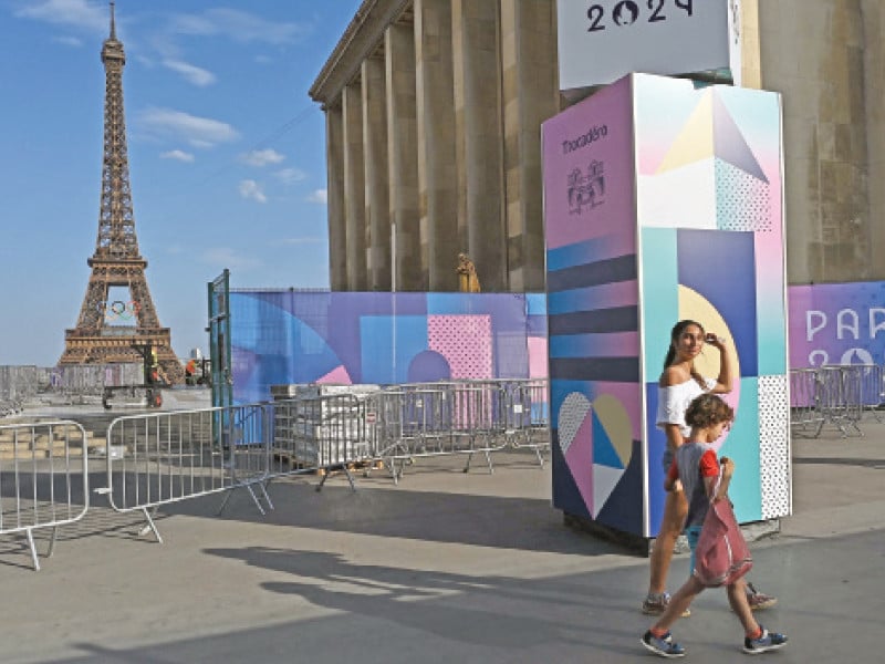 pedestrians walk past fences closing off access to the trocadero with the eiffel tower seen in the background ahead of the paris 2024 olympics photo afp