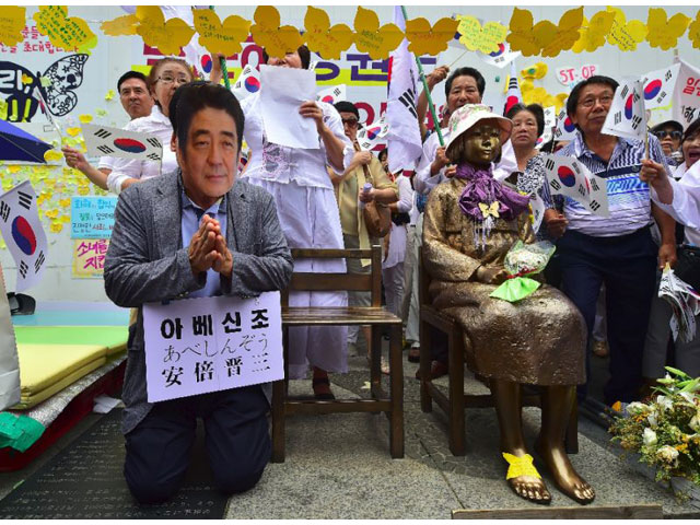 a man left wearing a mask of japanese prime minister shinzo abe kneels down in a mock apology next to the statue right of a teenage girl symbolising former quot comfort women quot in seoul on august 15 2016 photo afp