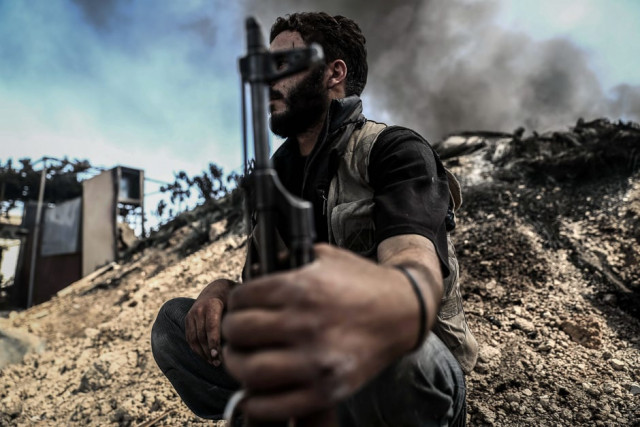 a fighter from the jaish al islam islam army sits near smoke billowing on the front line which they use to take cover in the village of tal al siwan area of the rebel held stronghold of douma on the outskirts of damascus photo afp