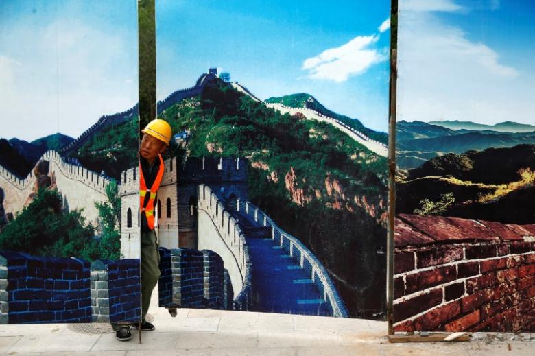 a worker looks through the fence of a construction site that is decorated with pictures of the great wall at badaling north of beijing china photo reuters