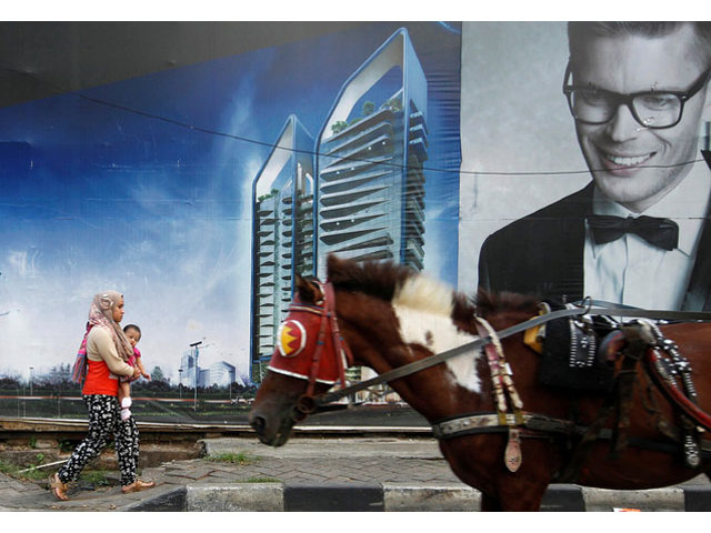 a woman holds her baby as she walks in front of a billboard of a new apartment in jakarta indonesia july 26 2016 photo reuters